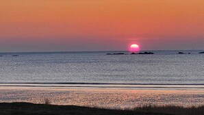Solnedgang over et roligt hav med landmasser i det fjerne.