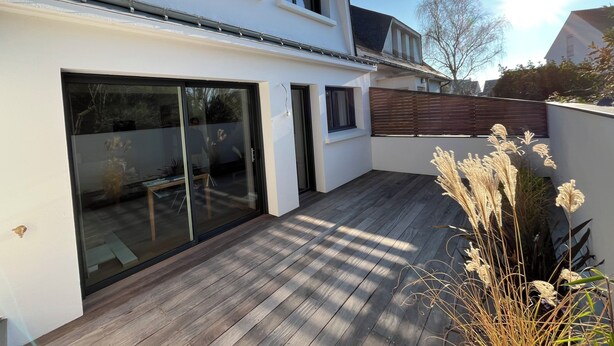 Et moderne hus med stor skydedør, træterrasse og en lukket baghave.