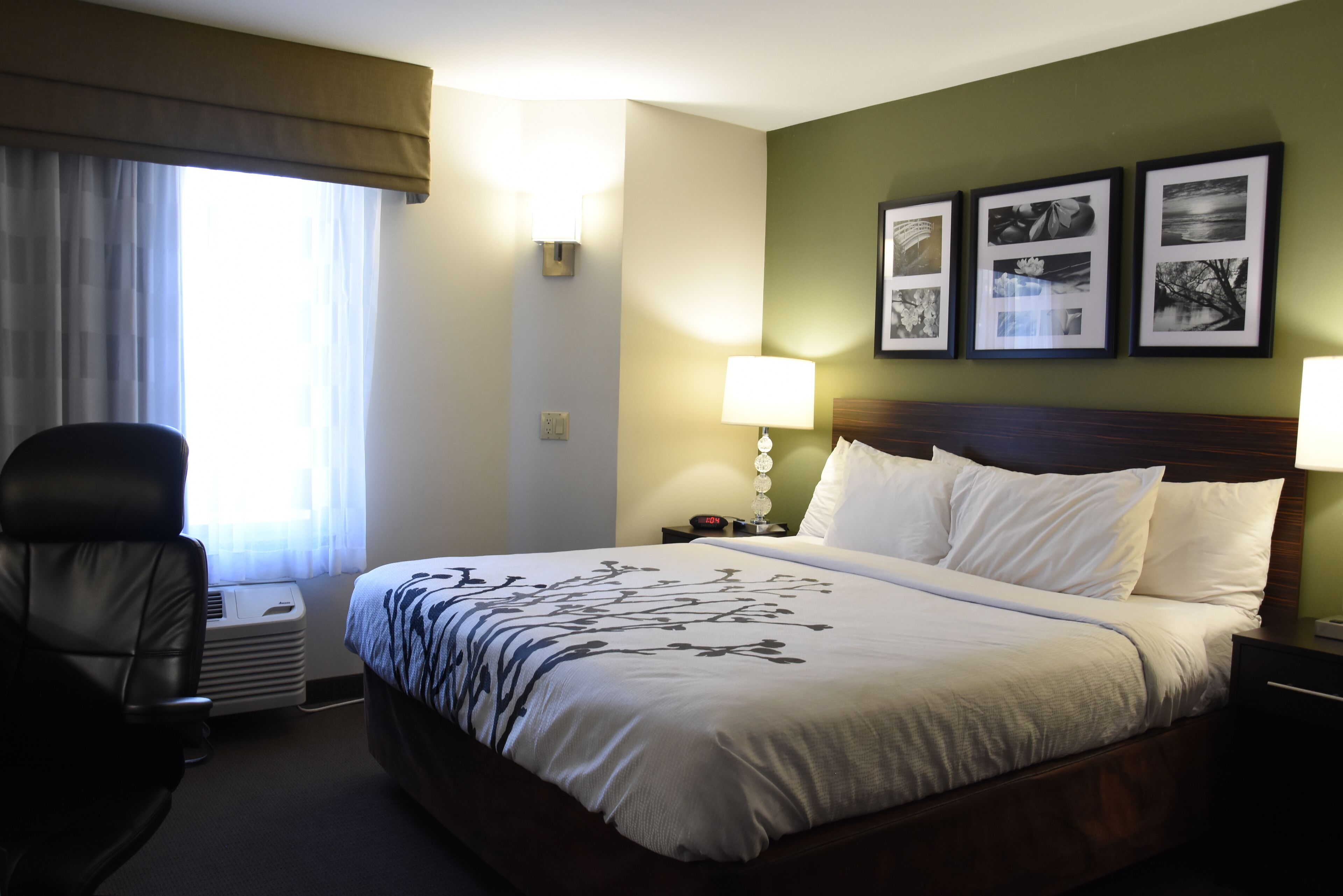 A hotel room with a large bed, a chair, a nightstand with a lamp, and framed pictures on the wall.