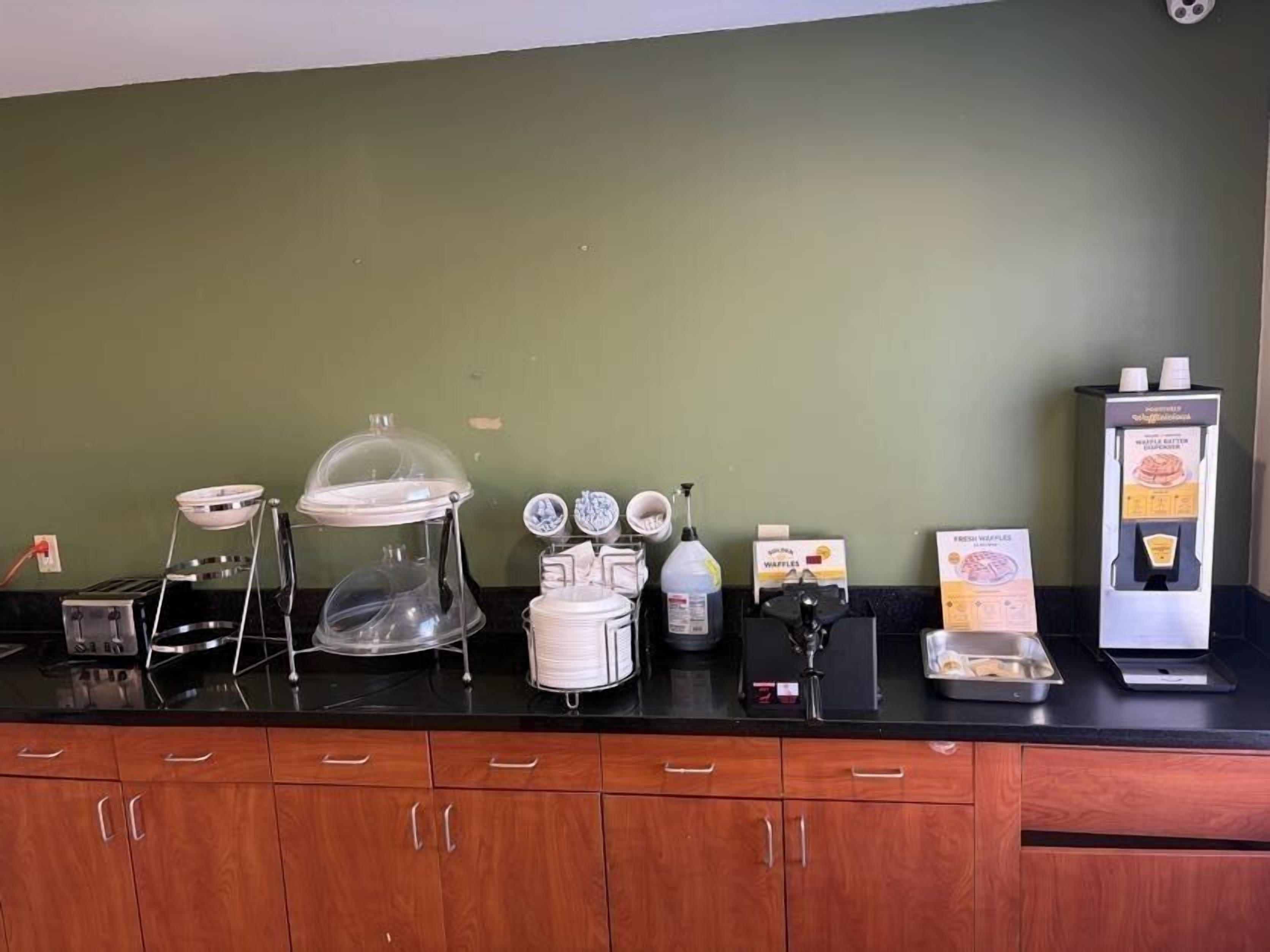 Uma bancada de cozinha com um aparelho para waffles, uma cafeteira e um dispensador de waffles.