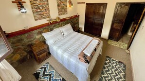 A bedroom with a stone headboard, a bed with white linens, a nightstand, a wooden wardrobe, and a hanging light fixture. - Lake view, comfortable artistic design (Ouirgane)
