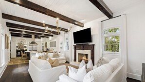 A spacious living room with a fireplace, white sofas, and a TV mounted on the wall. - Home with Private Pool and Courtyard (Rosemary Beach)