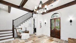 A spacious foyer with a stone floor, a wooden staircase, and a chandelier. - Home with Private Pool and Courtyard (Rosemary Beach)