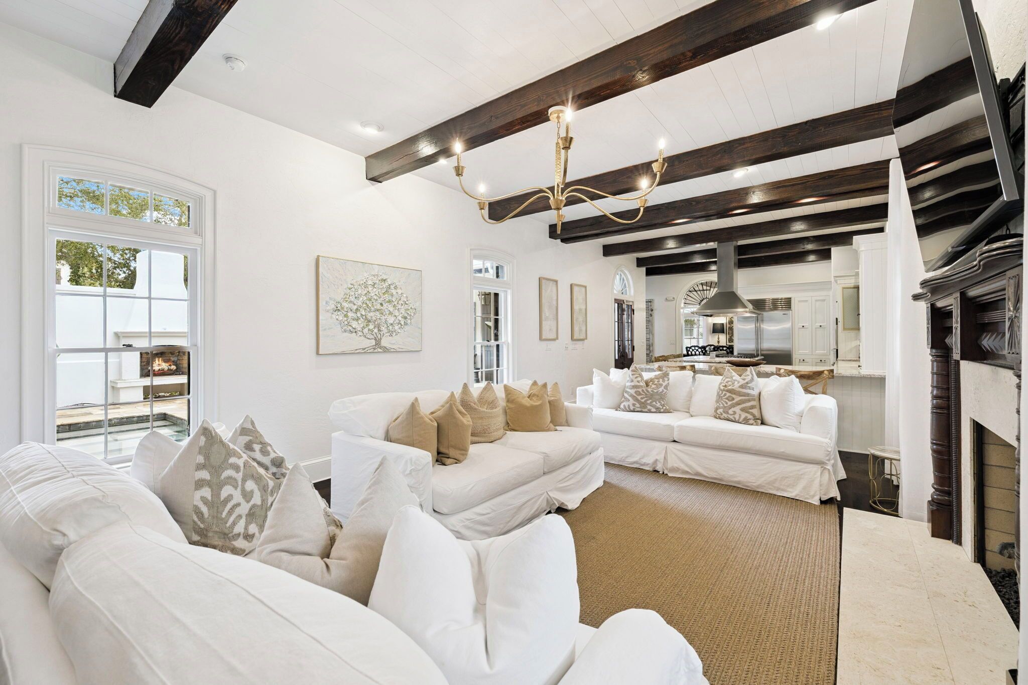 A spacious living room with a white sofa set, a fireplace, and a large window.