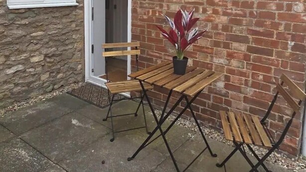 A brick house with a stone wall, a wooden table with chairs, and a potted plant. - 2 Bed Well Equipped For Contractors Pet Friendly (Edinburgh)