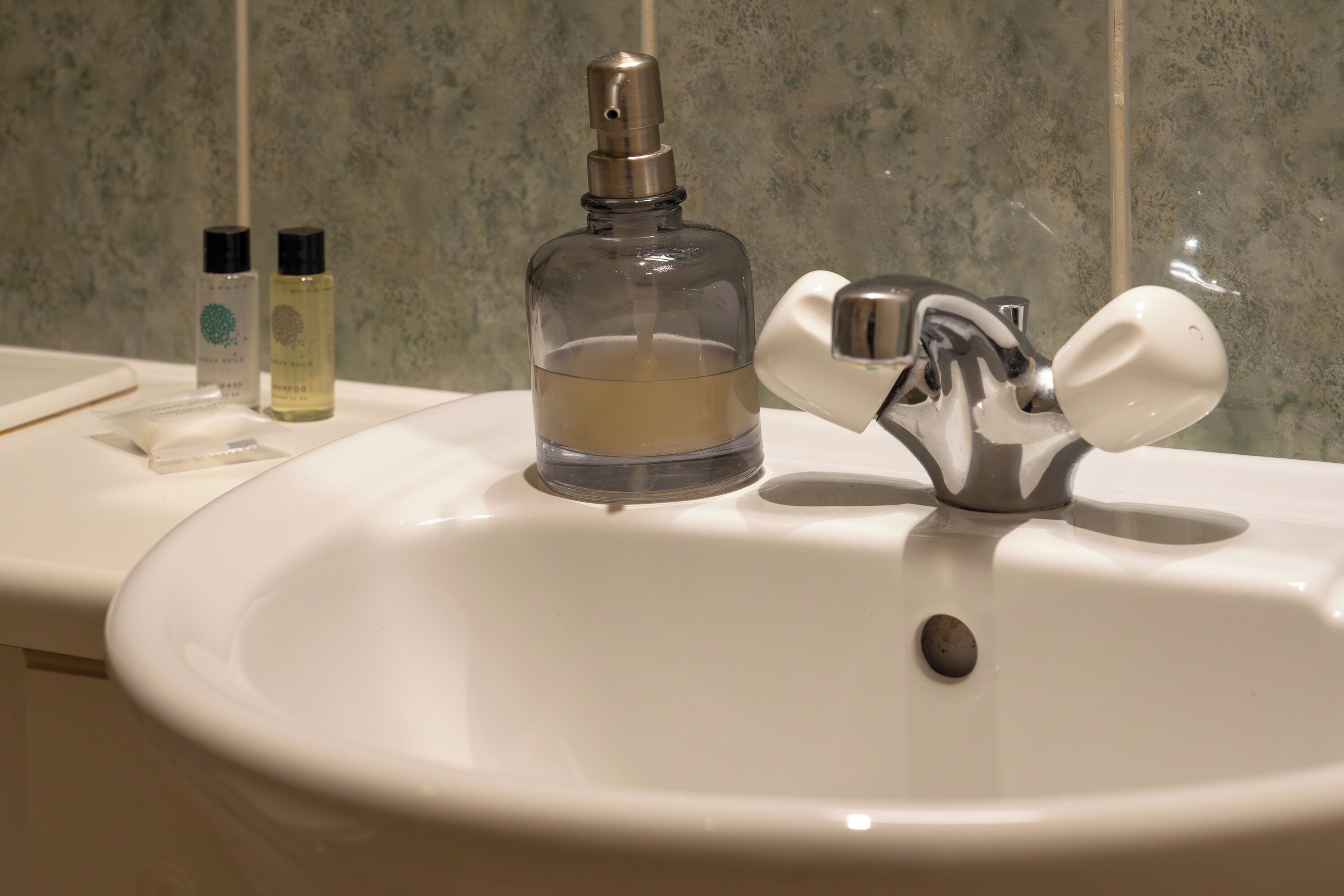 A bathroom sink with a chrome faucet and a bottle of liquid soap.
