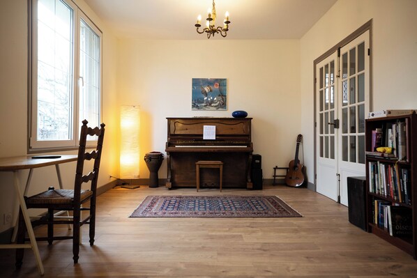A room with a piano, a chair, a rug, a bookshelf, and a door.