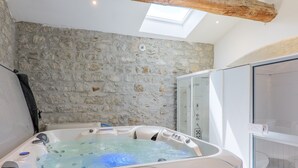 Ein Whirlpool mit Bedienfeld, einer Steinwand und einer Duschkabine aus Glas.