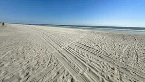 Ein sandiger Strand mit Radspuren und einem wolkenlosen, blauen Himmel.