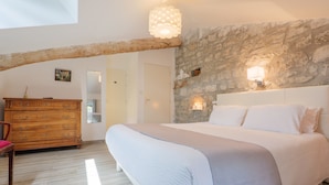 Une chambre avec un grand lit, une commode en bois, un mur en pierre et un plafond en pente.