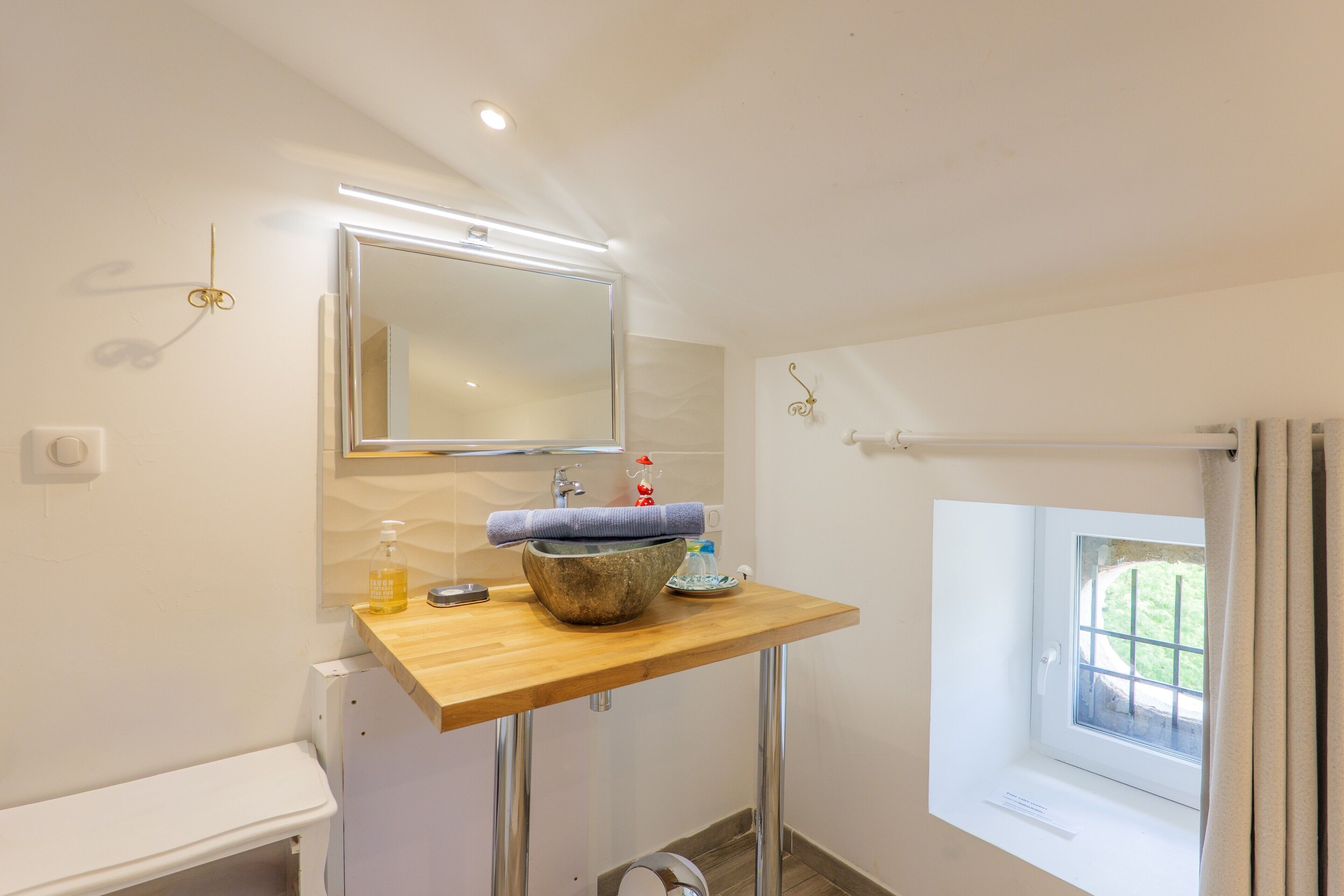 Une salle de bain avec un meuble-lavabo en bois, un miroir, une fenêtre et un porte-serviettes.