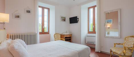 Un dormitorio con una cama grande, una silla, un escritorio, un televisor y una ventana.