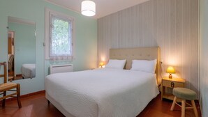 Un dormitorio con una cama grande, lámparas de noche, una mesita de noche de madera y un taburete pequeño.