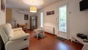 Una sala de estar con sofá, una mesita, refrigerador, televisor y puerta que da a un área exterior.