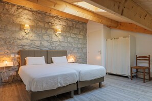 A double bed with a stone wall backdrop, two bedside lamps, a wooden ceiling, and a wooden chair. - Villa 'Le-joie' with Shared Pool, Wi-Fi, and Air Conditioning (Saint-Alban-Auriolles)