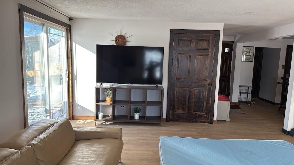 Un salon avec un grand téléviseur à écran plat, un canapé, un matelas bleu et une porte en bois.