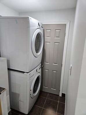 A laundry room with stacked washers and dryers, a door, and tiled flooring.