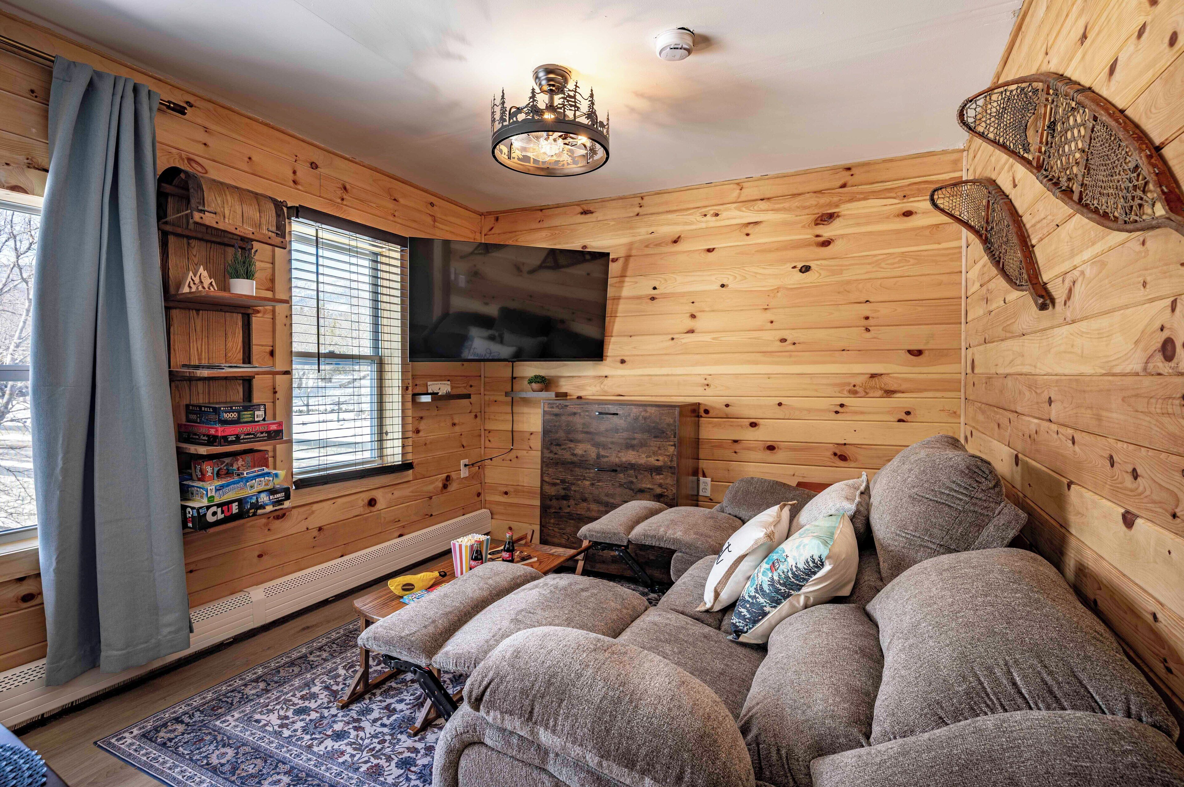 A cozy cabin interior with a sofa, television, wooden walls, and a fireplace.
