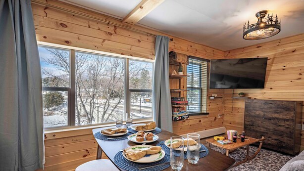 Un intérieur en bois avec une table à manger dressée pour le repas, une cheminée et un téléviseur fixé au mur.