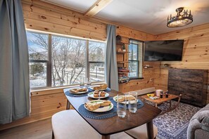 A wooden interior with a dining table set for a meal, a fireplace, and a television mounted on the wall. - Condo with Ausable River View & Backyard (Wilmington)