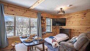L’intérieur chaleureux d’un chalet comprend un coin repas, un canapé et un téléviseur fixé au mur.