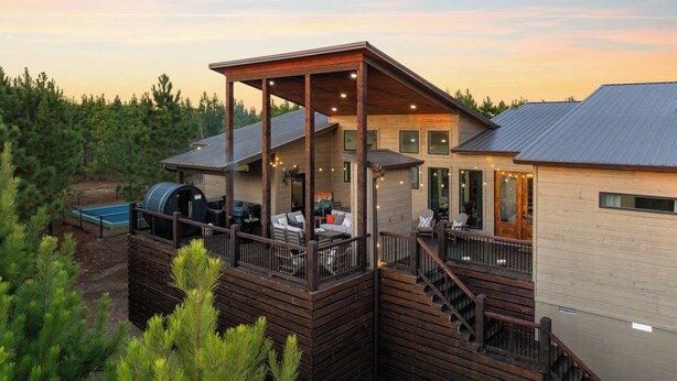Una casa de dos pisos con terraza de madera, zona de estar al aire libre y una parrilla.