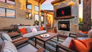 Un espacio al aire libre acogedor con una chimenea de piedra, muebles de madera y un televisor montado en la pared.