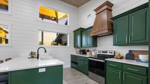 Una cocina con armarios verdes, encimera blanca y techo de madera.