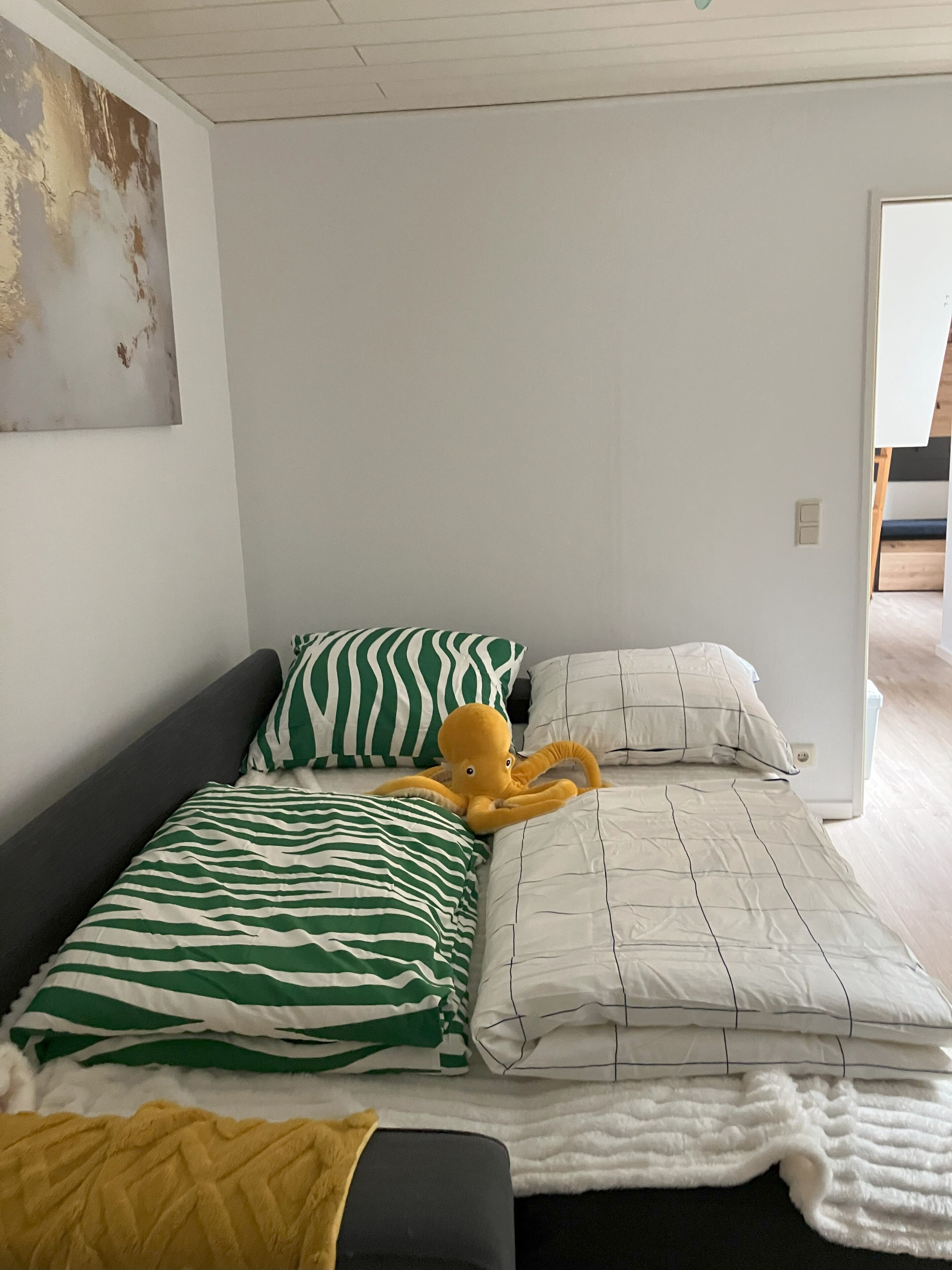 A bedroom with two beds, one with green and white striped bedding and the other with white bedding. There is a yellow plush octopus toy on the bed with green and white striped bedding.