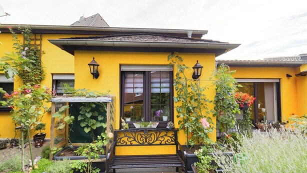 Un edificio giallo con un balcone nero e piante in vaso.