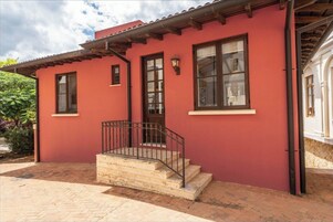 Un edificio rojo con entrada de ladrillo, un pequeño porche y una ventana con baranda de metal.