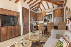 Una cocina amplia con armarios de madera, un televisor grande y un comedor con sillas de mimbre.