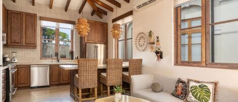 A spacious kitchen with wooden cabinets, a dining area with wicker chairs, and a living room with a sofa and decorative pillows.