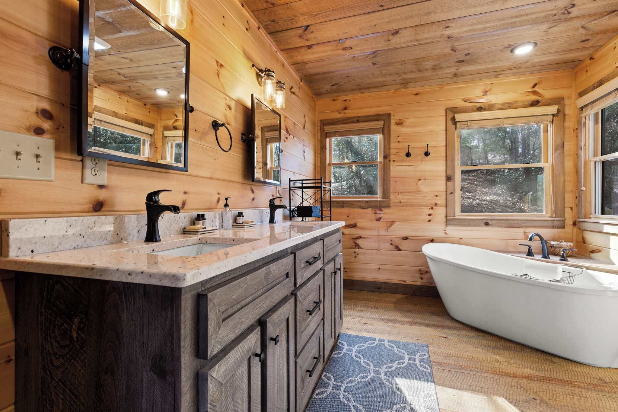 A wooden cabin bathroom with a freestanding bathtub, a large mirror, and a vanity with a sink.