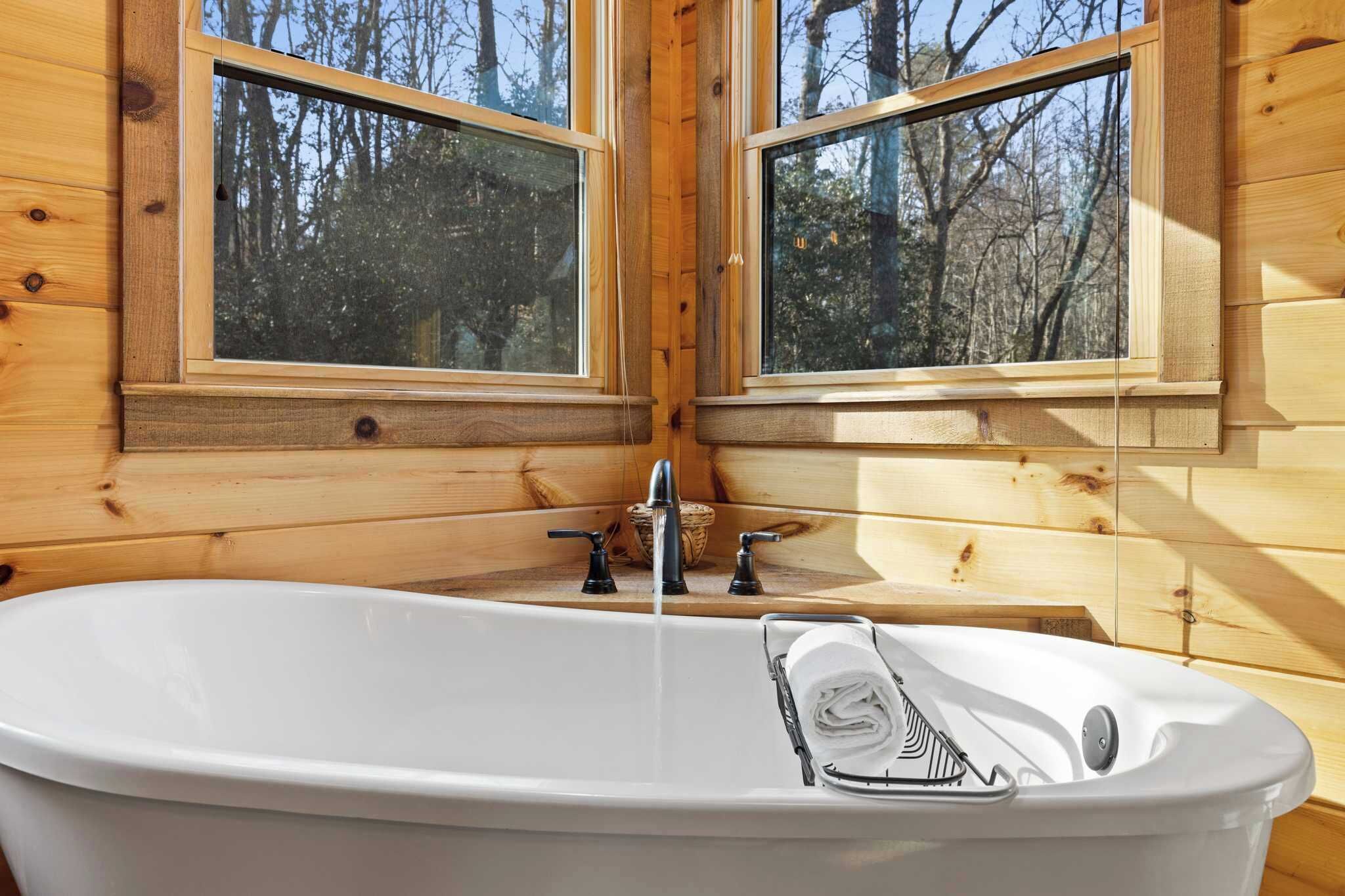 Eine Holzhütte mit einer weißen Badewanne, zwei Fenstern und einem kleinen Waschbecken.