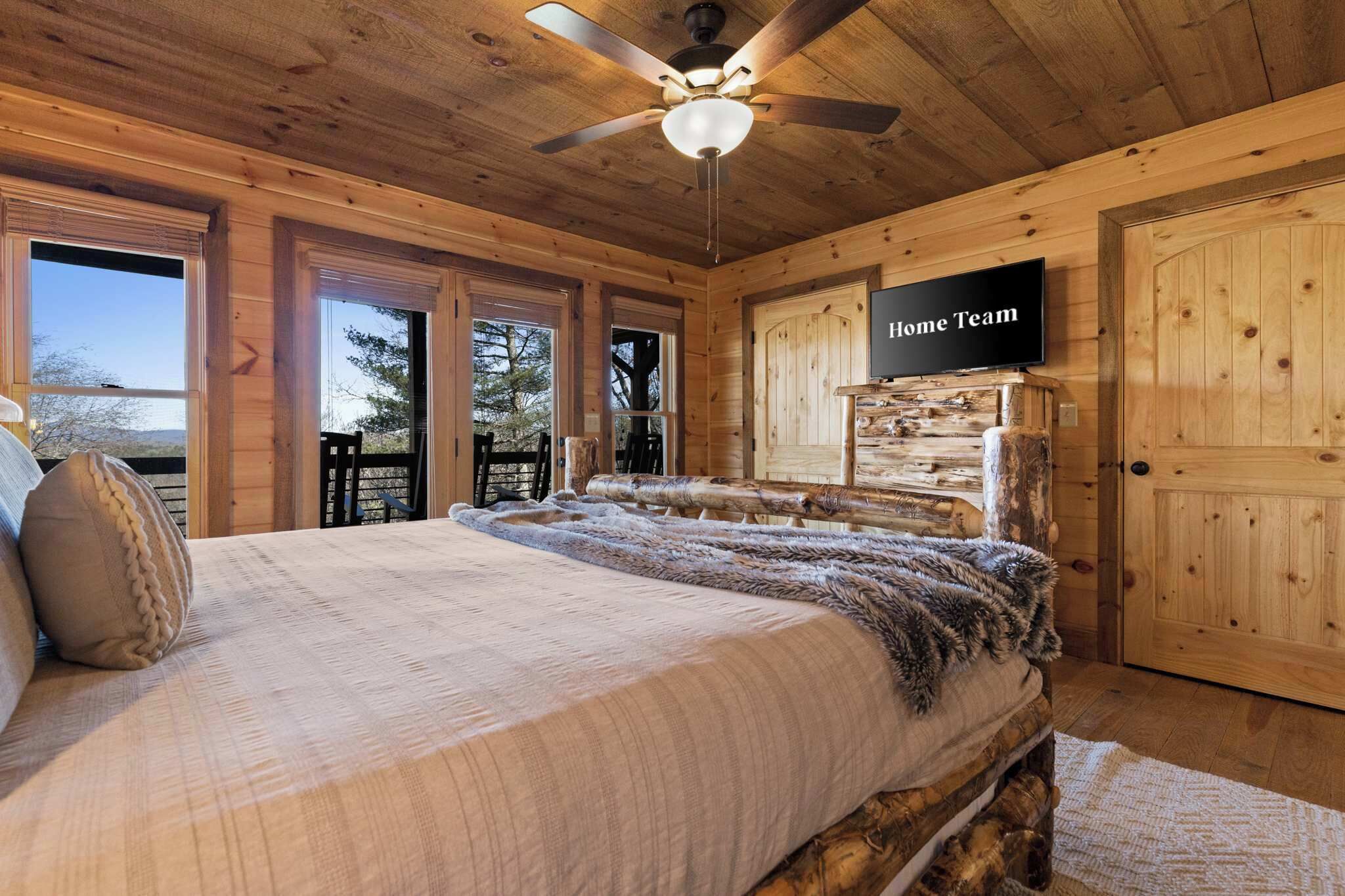 A wooden cabin bedroom with a bed, a ceiling fan, and a TV on the wall.