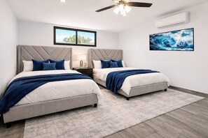 Ein Schlafzimmer mit zwei Betten, einem Deckenventilator, einer Klimaanlage, einem großen Fenster und einem an der Wand montierten Fernseher.