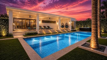 Une maison moderne dotée d’une piscine, de grandes fenêtres et d’un espace salon extérieur.