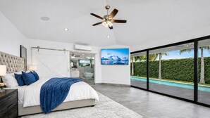 A modern bedroom with a large bed, a ceiling fan, and a view of a swimming pool through glass doors. - NEW Cabo 4BR Ocean View Villa - 50ft Pool Hot Tub (Cabo San Lucas)