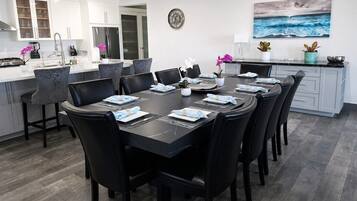 A modern kitchen with white cabinetry, a dining area with black chairs and a marble table, and a view of the ocean through a window.