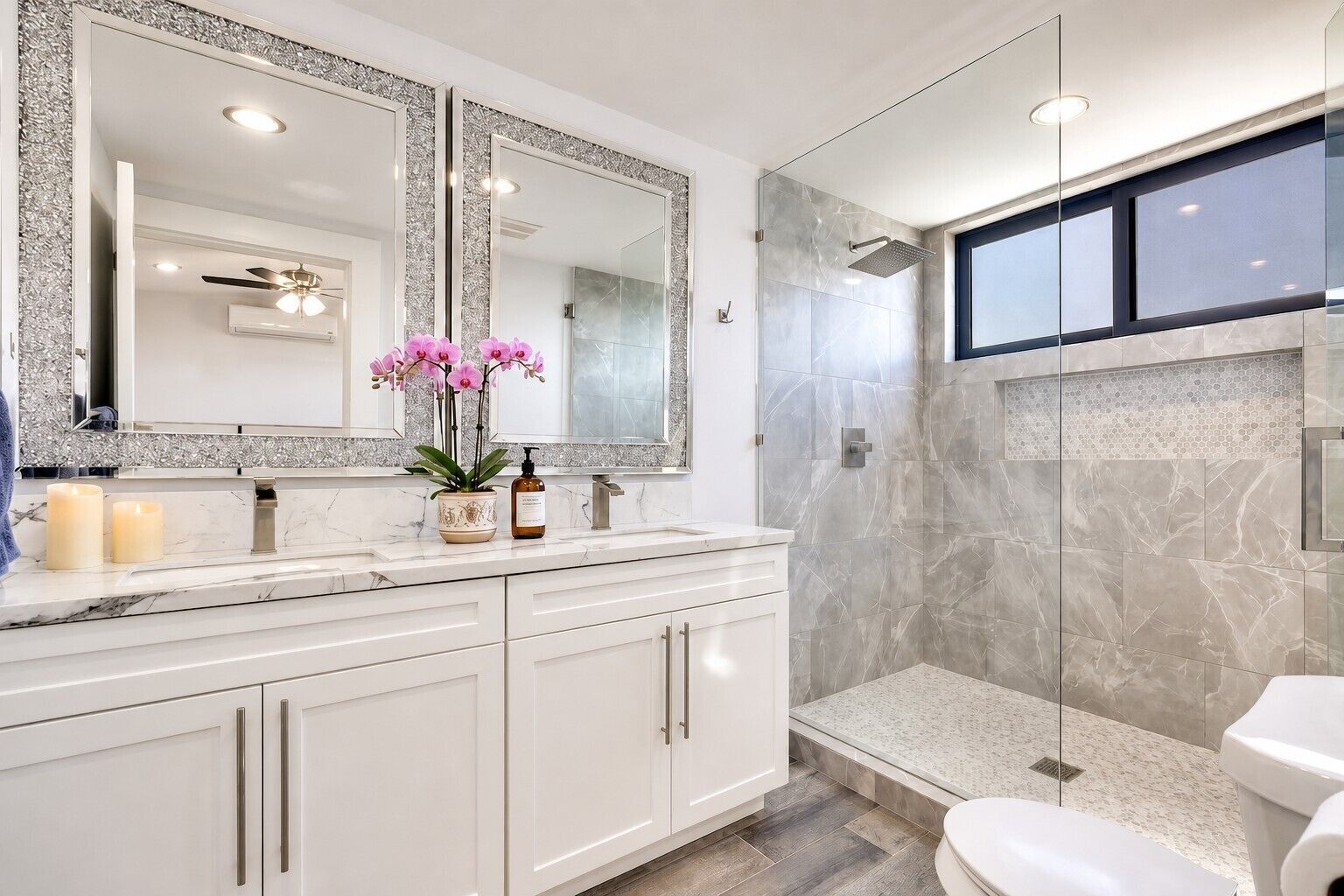 A modern bathroom with a large mirror, a shower enclosure, and a vanity with a marble countertop.