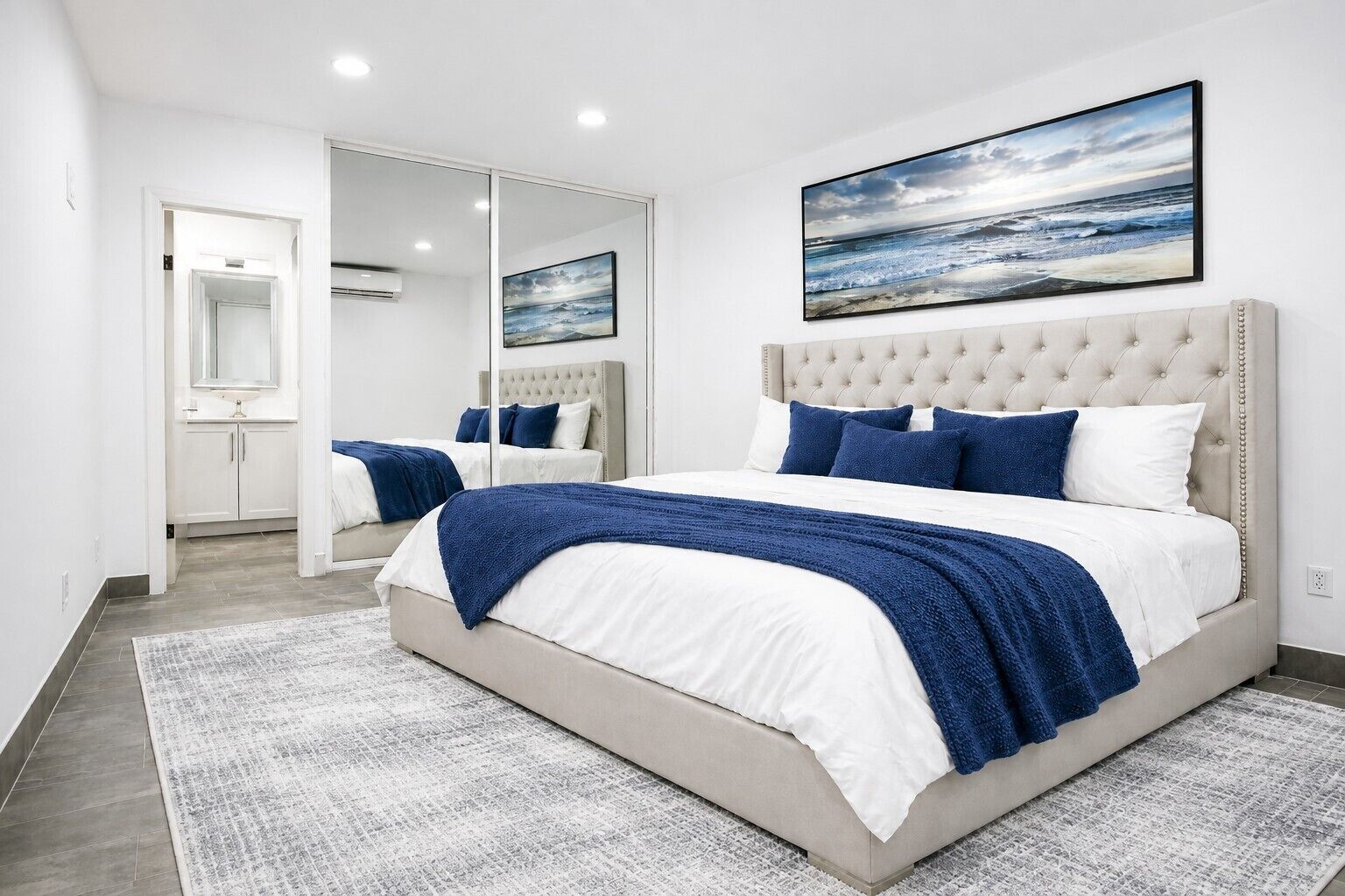 A bedroom with a large bed, a mirror, and a painting of the ocean.