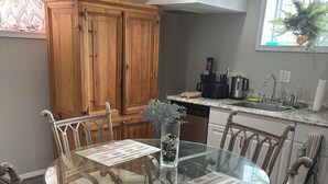 Uma área de refeições com uma mesa de vidro, cadeiras de vime e um armário de madeira ao fundo.
