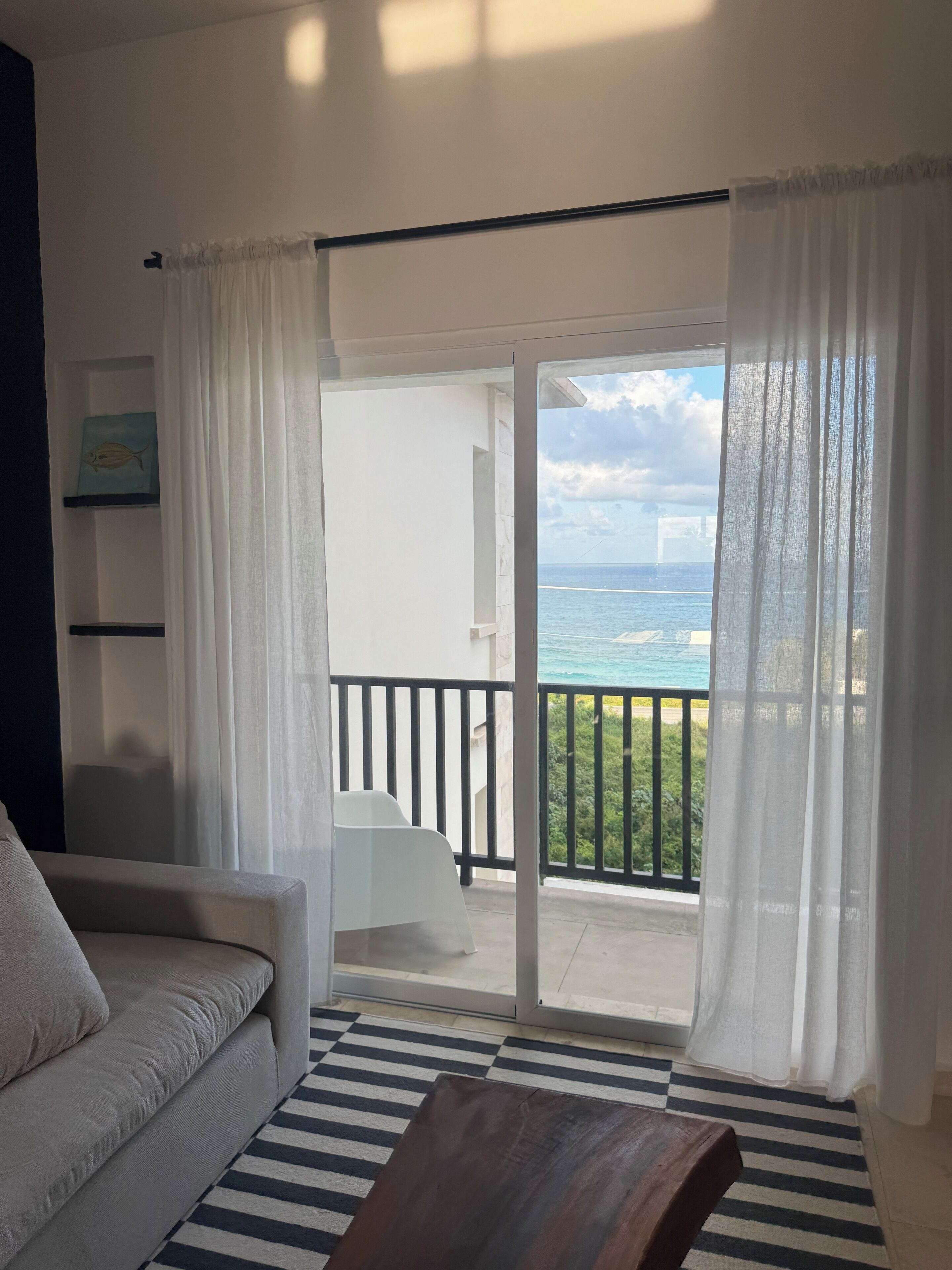 A room with a sofa, a wooden table, and a view of the ocean through a glass door.