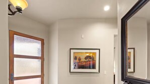 A hallway with a wooden door, a framed painting, a black bench, and a tiled floor.