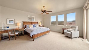 A bedroom with a wooden bed, a desk, a chair, a ceiling fan, and large windows.