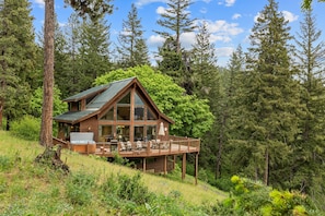 A cabin with a deck, surrounded by forest.