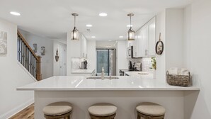 A modern kitchen with a large island, wooden stools, pendant lighting, and white cabinetry. - Lowcountry Luxury,Updated Shipyard Townhouse, Steps to Pool, 8 Min Walk to Beach, Grill, Golf View (Hilton Head Island)