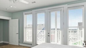 A bedroom with a large bed, a ceiling fan, and a view of the city through large windows. - 2-bedroom condo, sleeps 6, in adorable Branson with cool AC and gym access. (Branson)