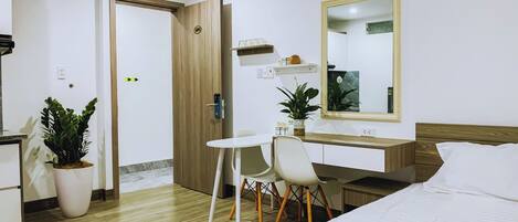 A hotel room with a bed, a desk, a chair, a mirror, and a potted plant.